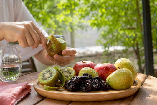 Bowl of fresh fruits aiding digestion with hand peeling kiwi