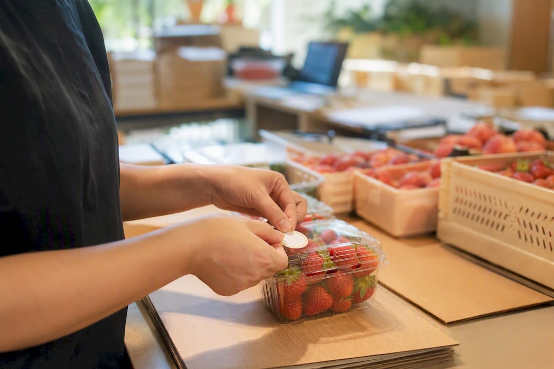 Hands applying country of origin label to fruit package